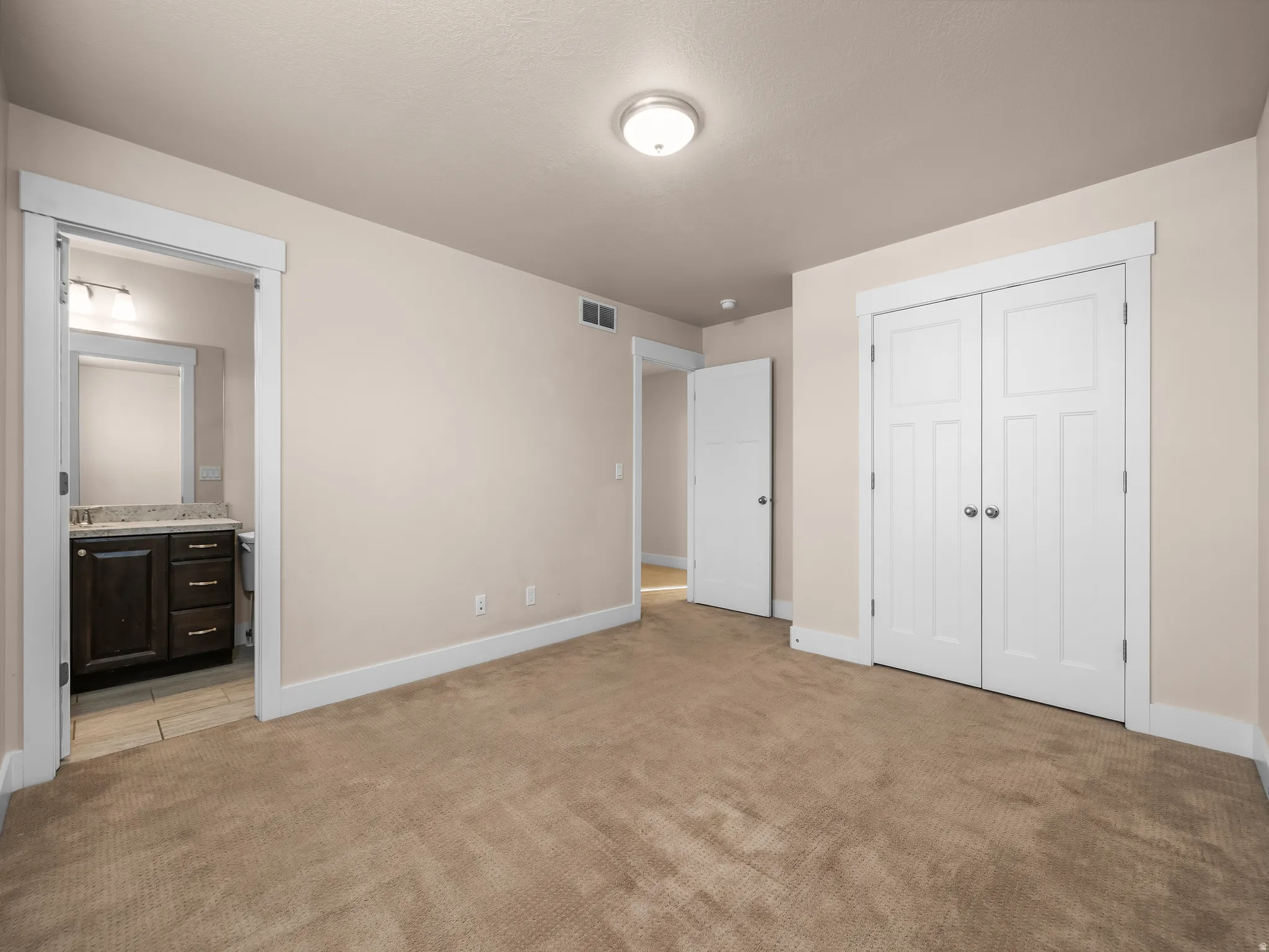 Neutral tone wall color, recessed ceiling light fixture, plush carpet flooring, white trim details, and a dark wood finish vanity with a light-colored countertop