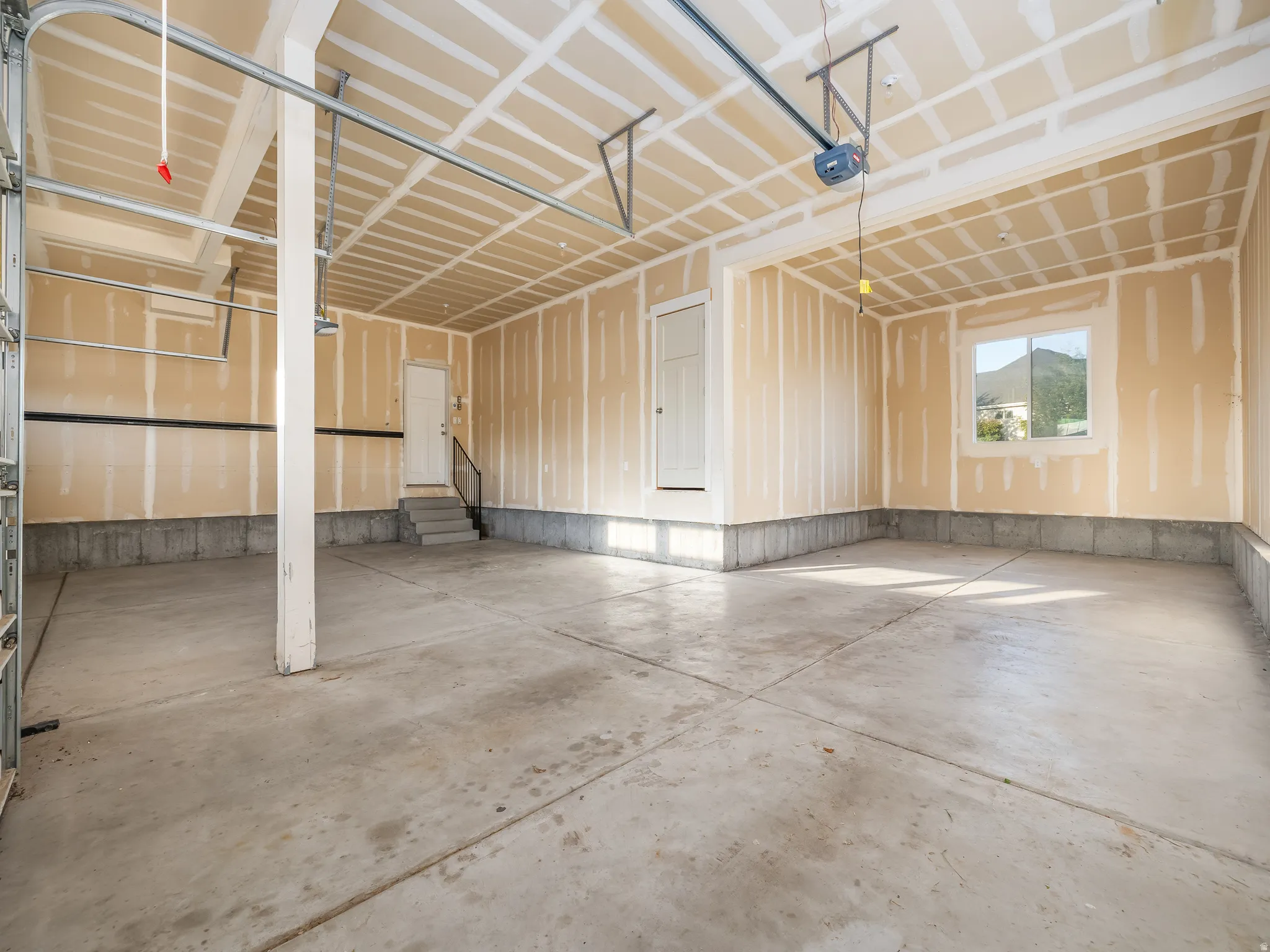 Spacious garage featuring a concrete floor, overhead garage door track system, and interior access door with stairs