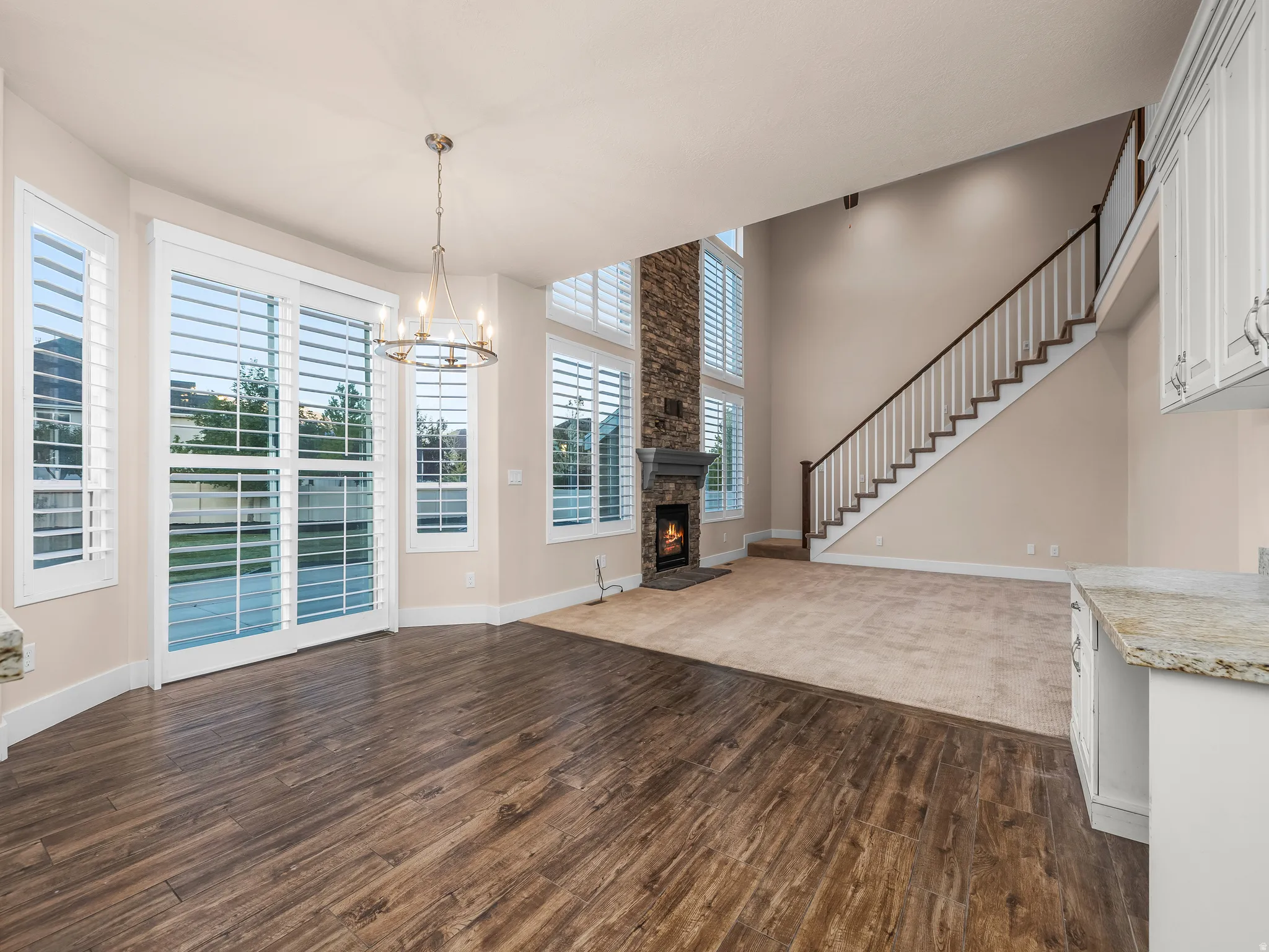 Wood-finish flooring, white plantation shutters, stone fireplace, vaulted ceiling, and a staircase with white balusters