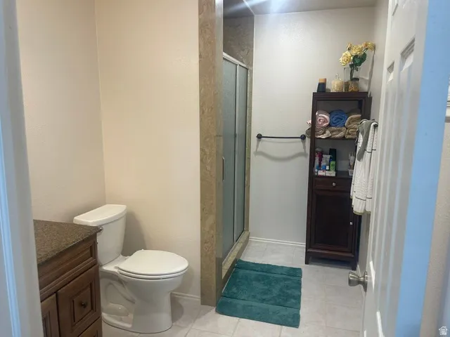 Tiled flooring with a glass-enclosed shower, dark wood vanity, and a light-toned countertop