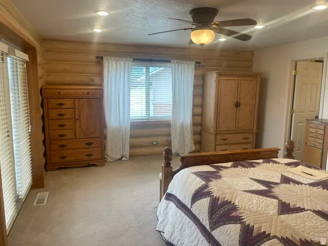 Log wall construction with recessed lighting, ceiling fan with integrated light, and wall-to-wall carpeting