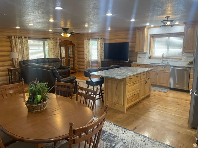 Kitchen featuring light wood-finish cabinetry, stainless steel dishwasher, and a center island with a stone countertop