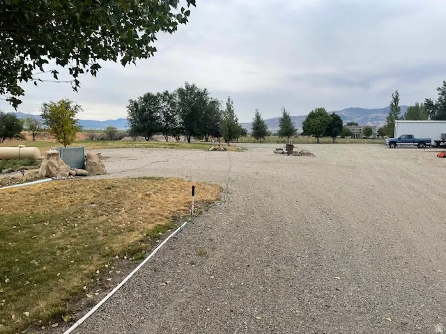 Expansive gravel lot with mature trees, established landscaping elements, and mountain backdrop