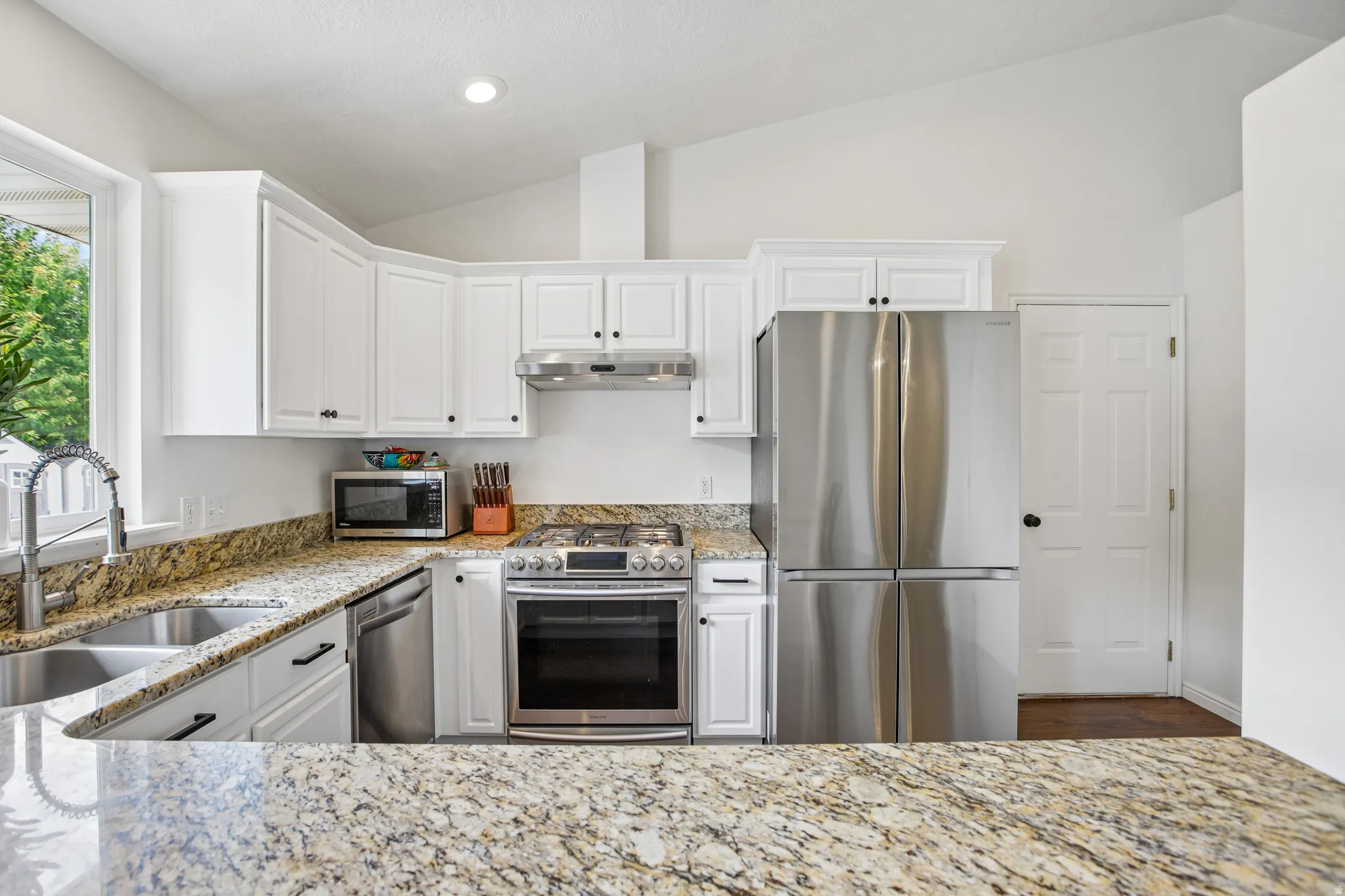 Kitchen featuring white cabinetry, granite countertops, stainless steel appliances, and a vaulted ceiling