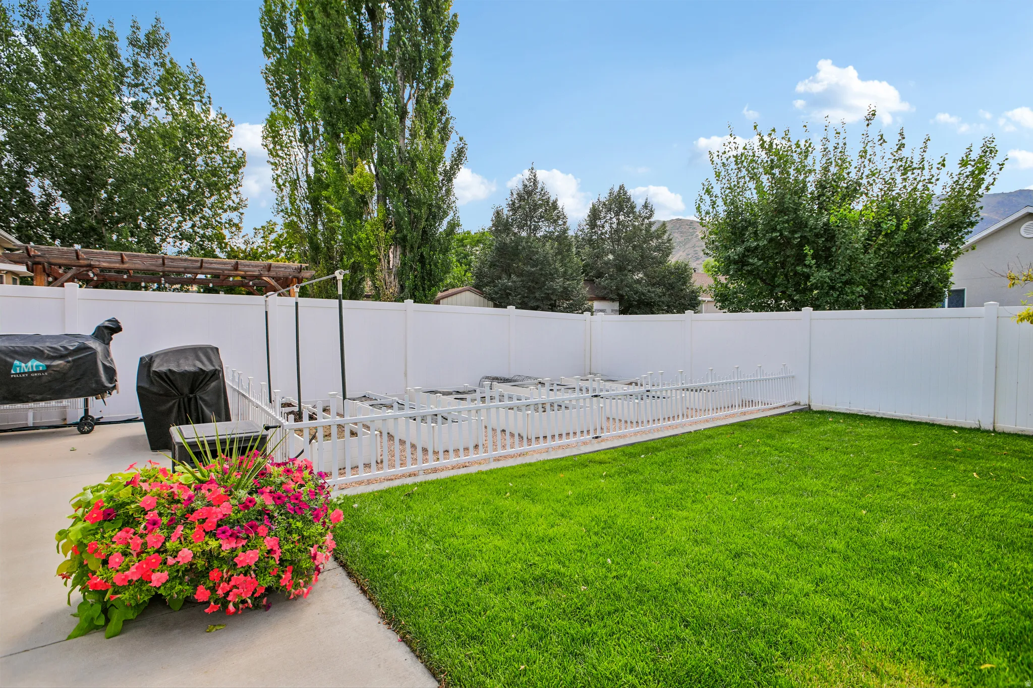Expansive backyard featuring a lush lawn, white privacy fencing, and a concrete patio