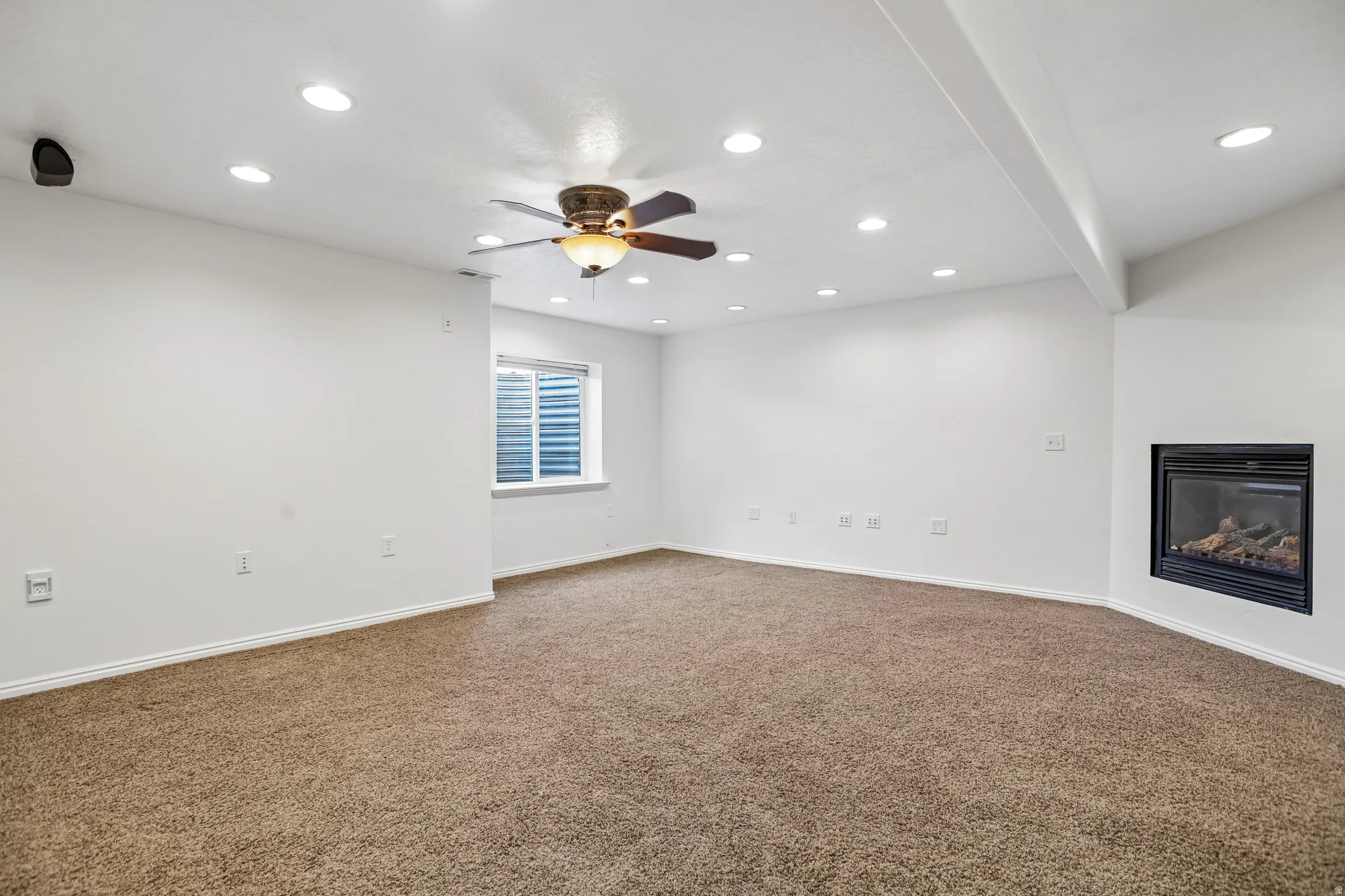 Recessed lighting, ceiling fan, built-in fireplace, wall-mounted speaker, and window with blinds