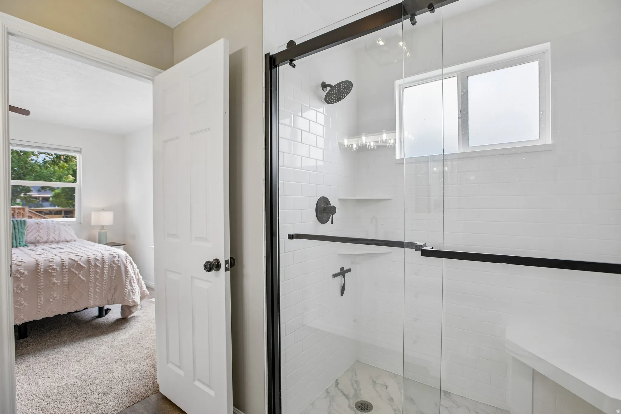 Glass-enclosed shower with matte black fixtures, white subway tile surround, integrated shelving, and a built-in bench