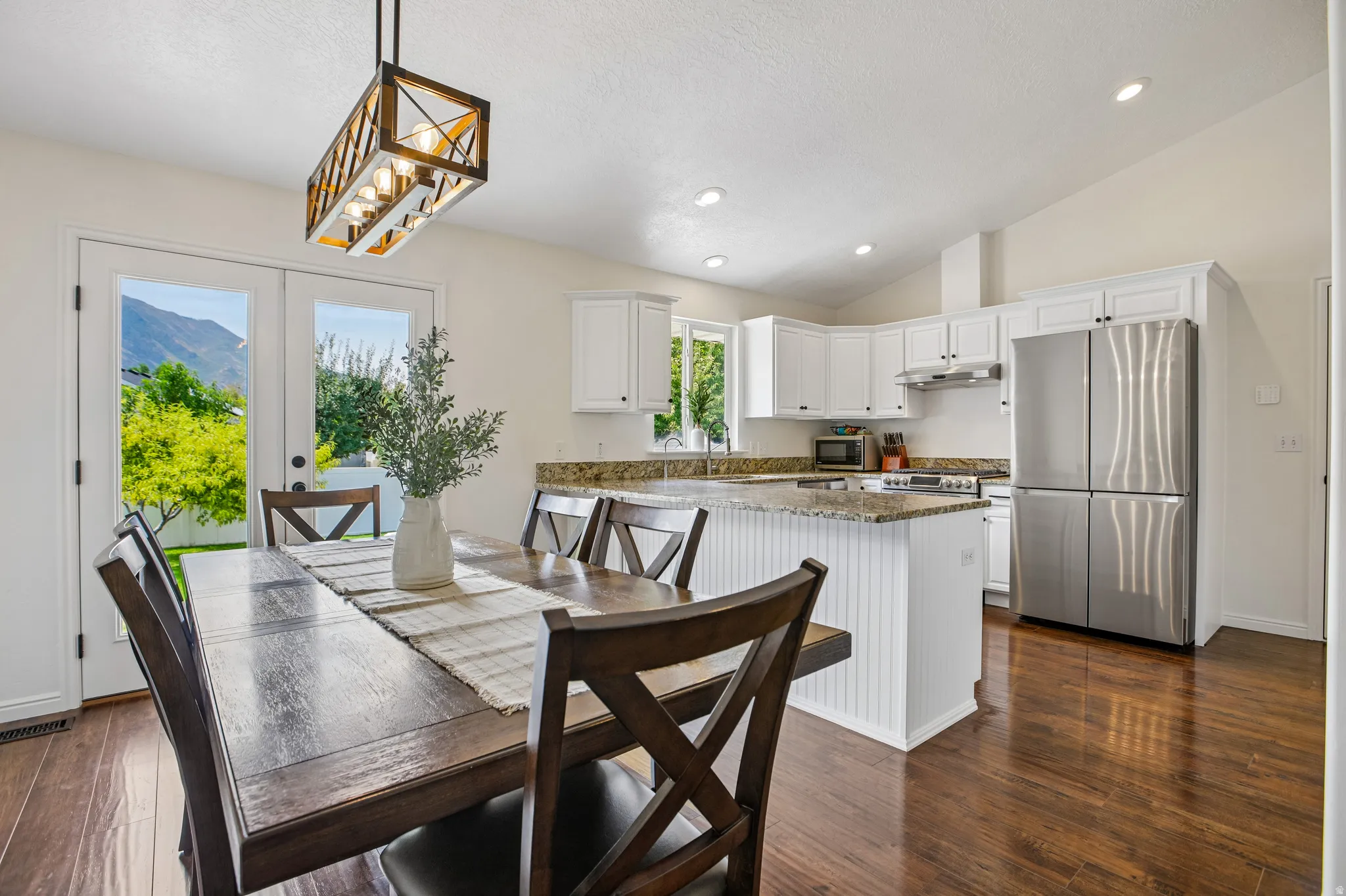 Kitchen and dining area featuring vaulted ceilings, wood-finish flooring, white cabinetry, a kitchen island with beadboard paneling, and stainless steel appliances