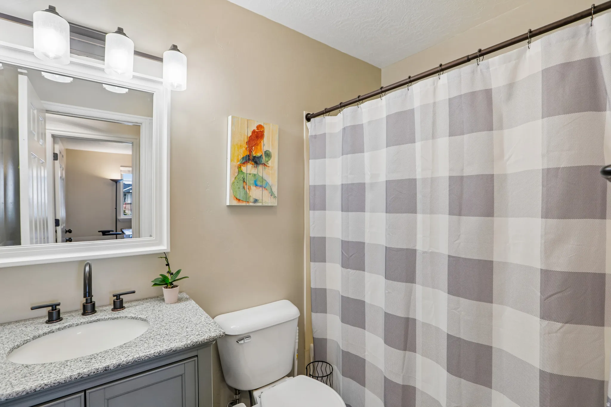 Vanity with granite countertop, undermount sink, matte black faucet, and framed mirror with integrated lighting