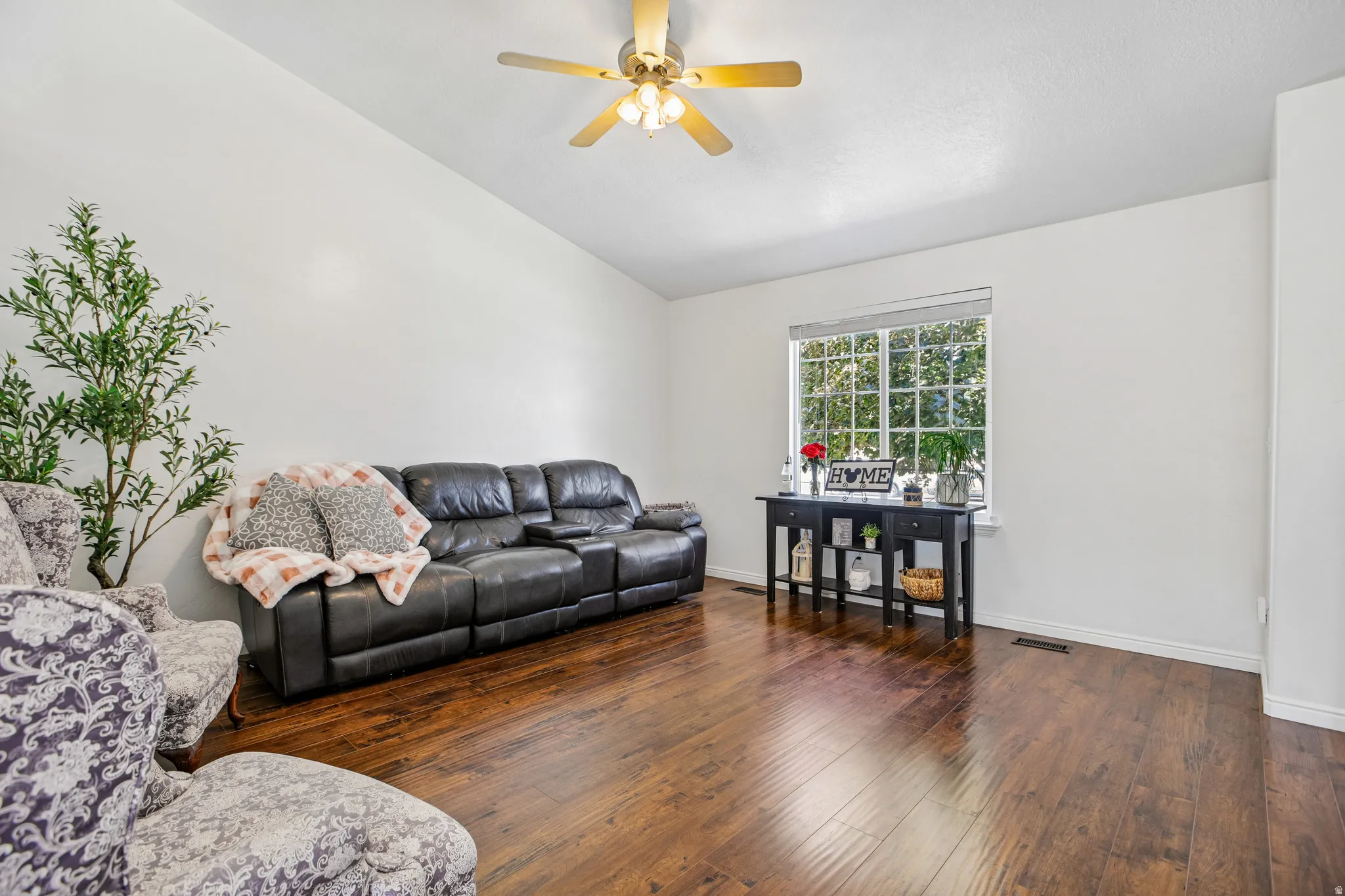 Vaulted ceiling with a ceiling fan, wood-finish flooring, and a large window