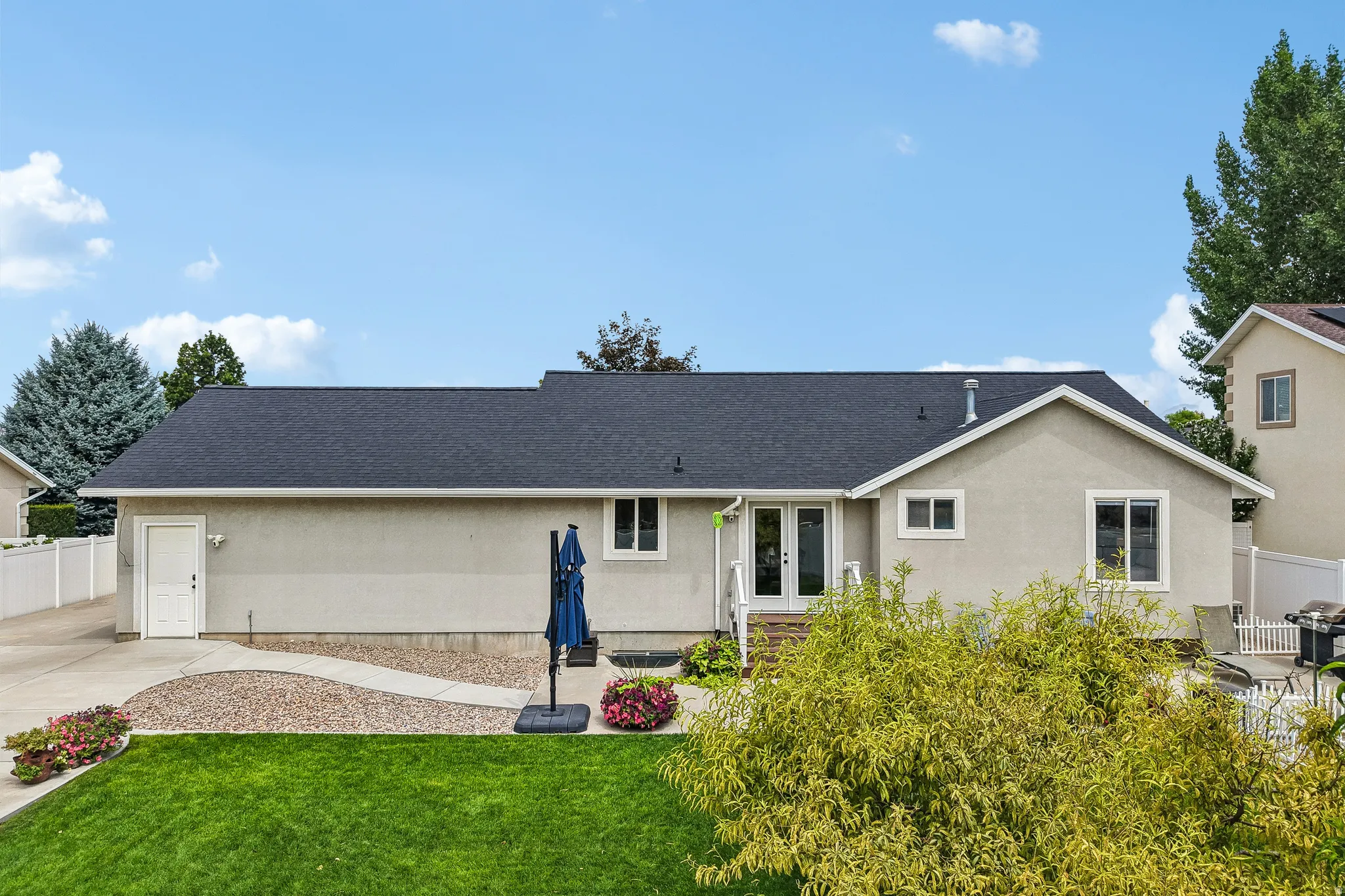 Expansive backyard featuring a manicured lawn, paved walkway, gravel landscaping, and mature trees