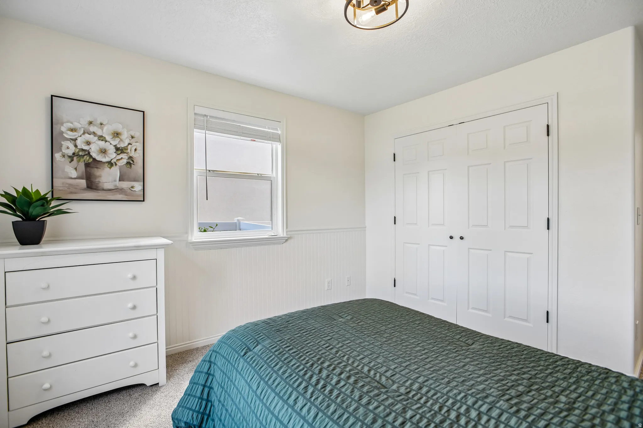 Carpeted flooring, paneled bifold closet doors, wainscoting, and a ceiling-mounted light fixture