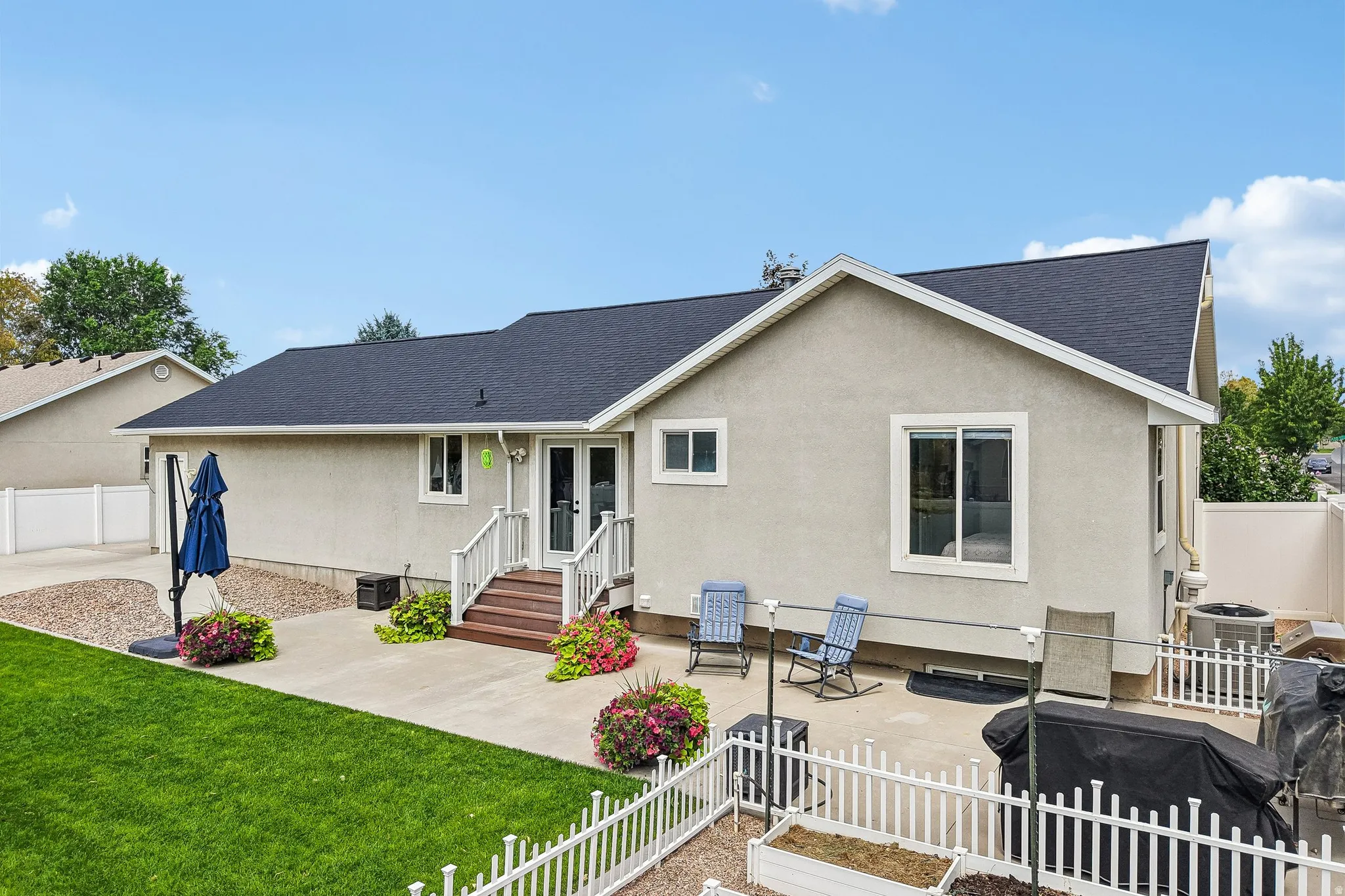 Backyard featuring a concrete patio, wood deck, white picket fence, and a manicured lawn