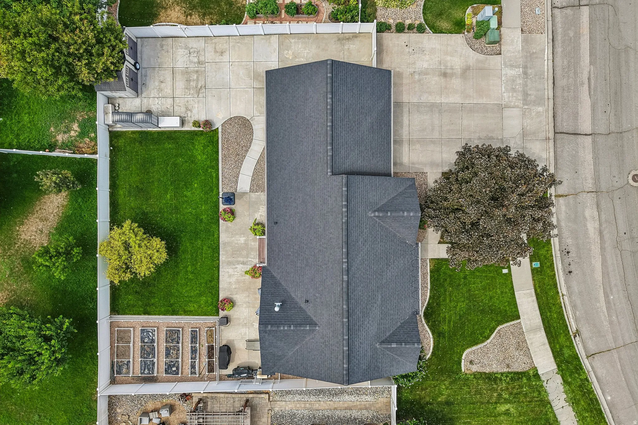 Private fenced backyard with a large concrete patio, manicured lawn, and raised garden beds
