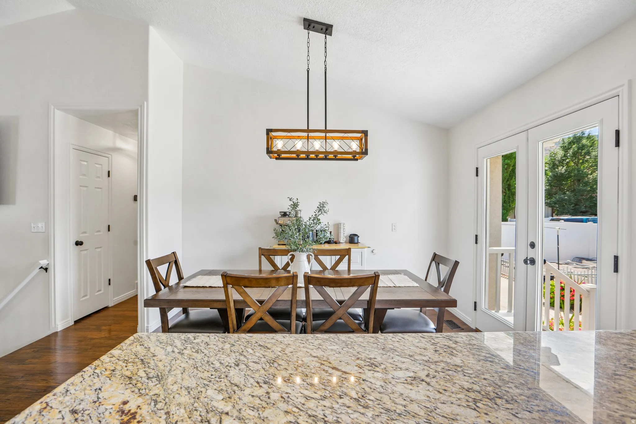 Textured granite countertop, vaulted ceiling, wood-finish flooring, French doors, and a rectangular pendant light fixture