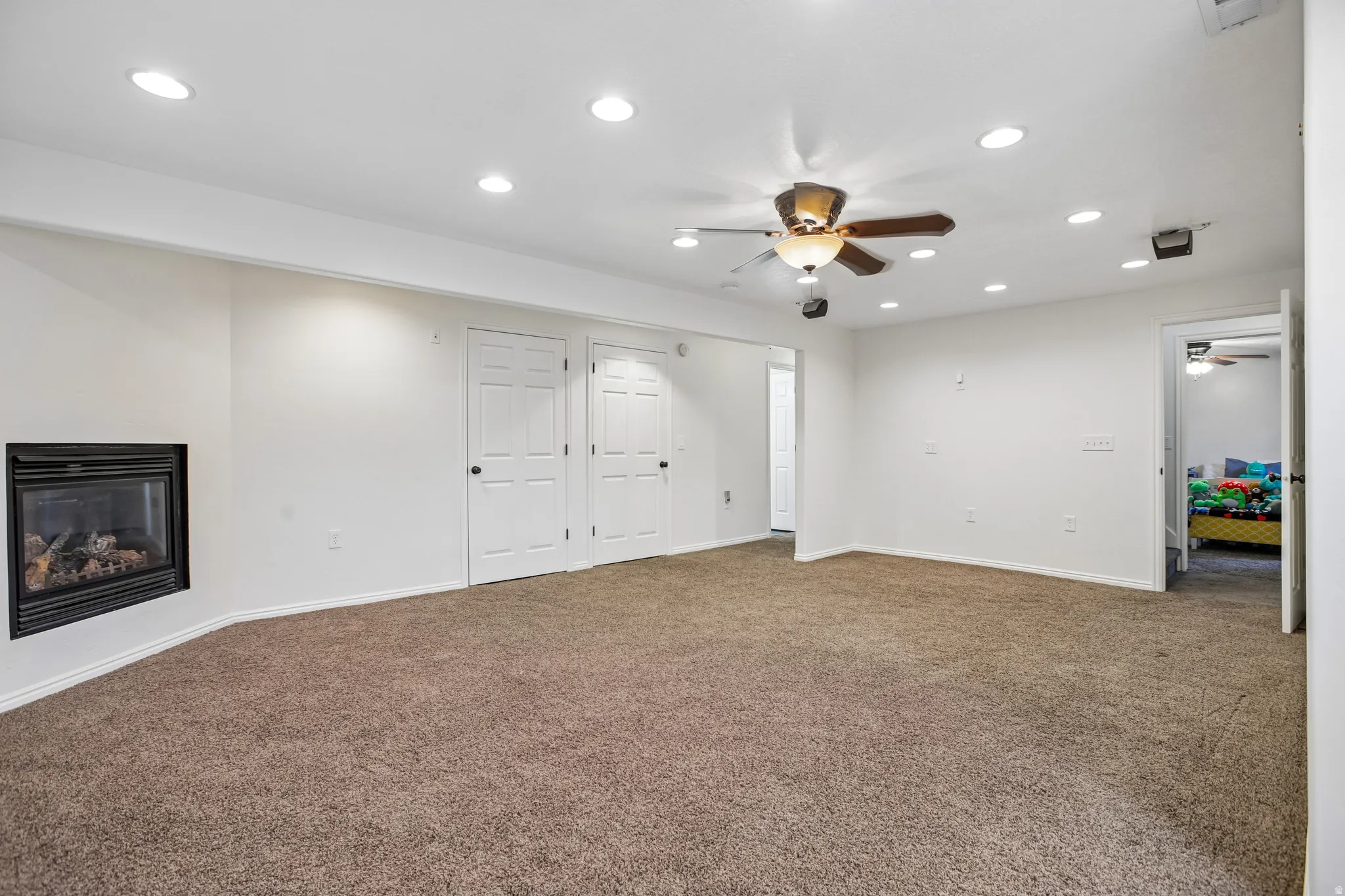 Recessed lighting illuminates the space, featuring a ceiling fan, gas fireplace, and carpet flooring