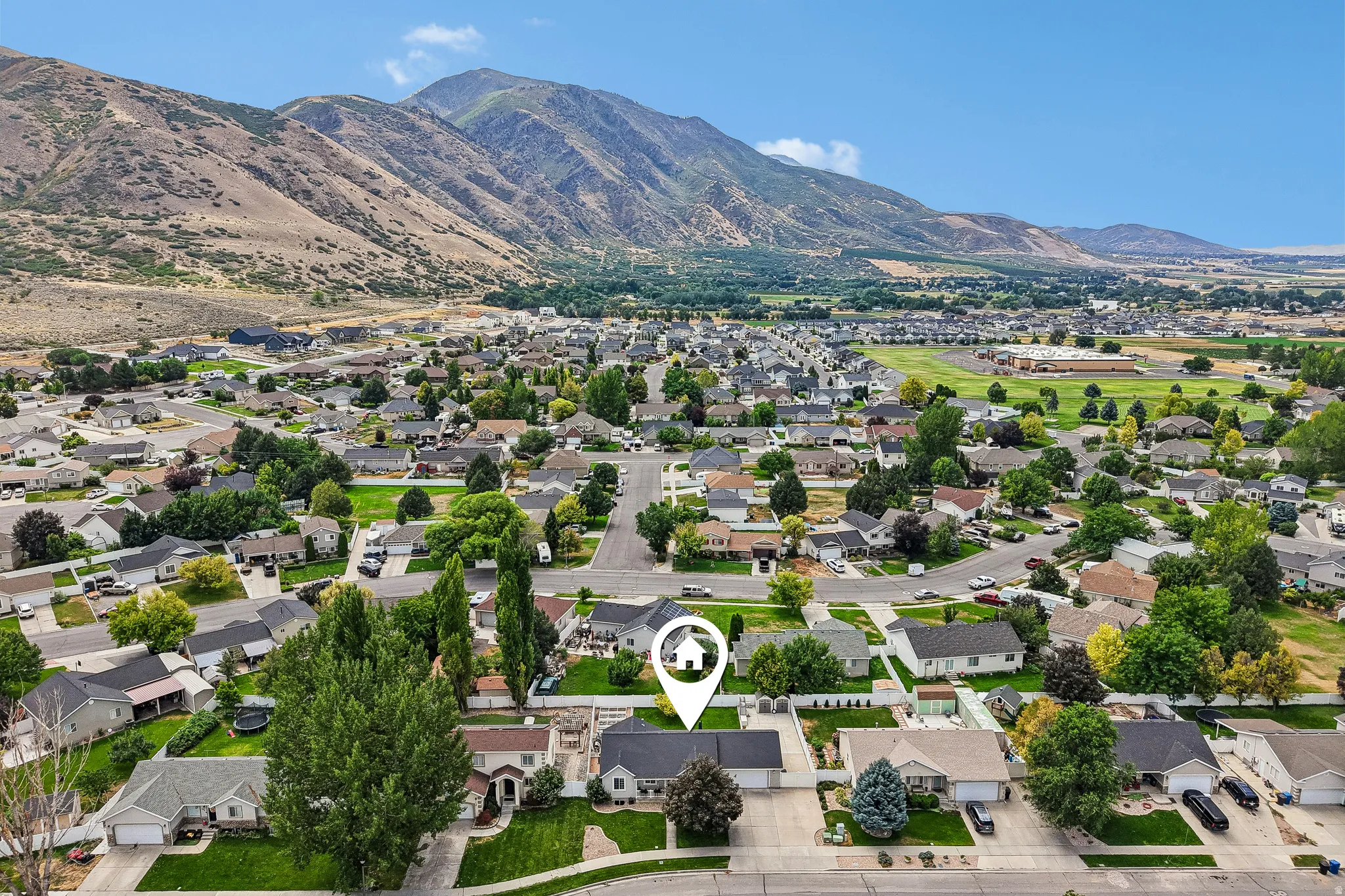 Residential neighborhood with mature trees, surrounded by mountainous terrain and open fields