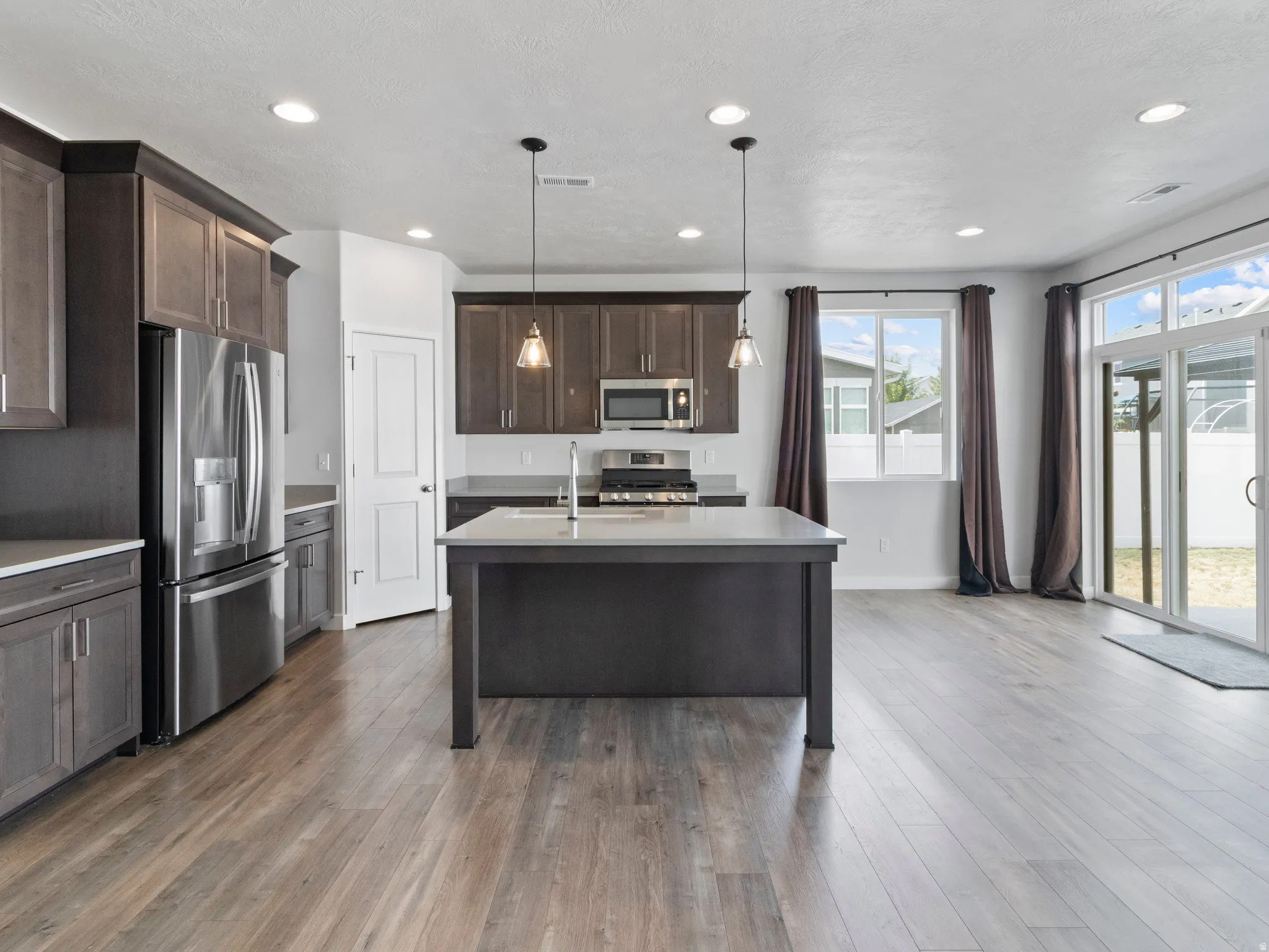 Kitchen featuring dark wood-finish cabinetry, stainless steel appliances, a center island with pendant lighting, recessed ceiling lights, and wood-finish flooring