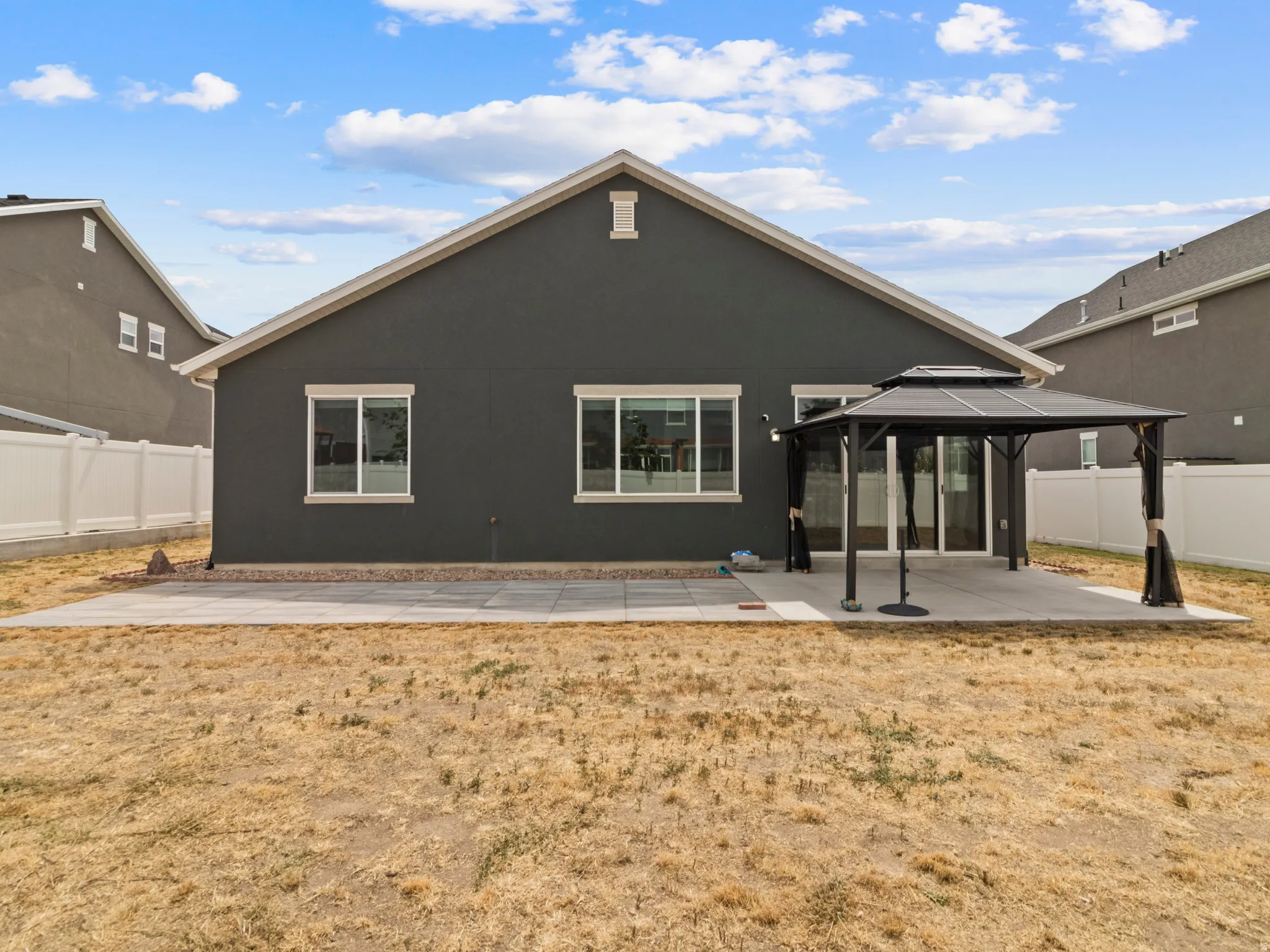 Rear exterior featuring a concrete patio, sliding glass doors, and multiple windows with white trim