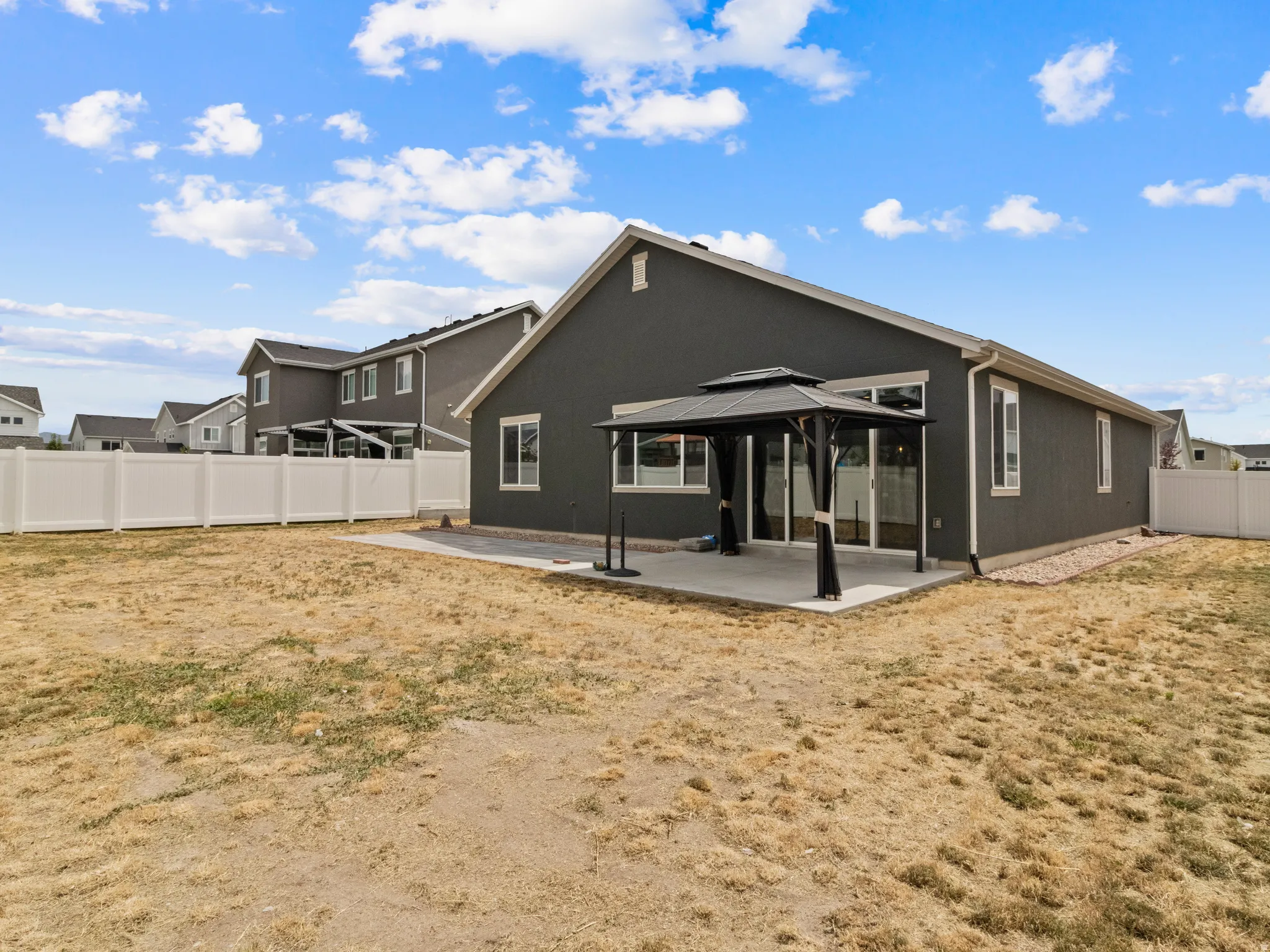 Rear exterior featuring a covered patio with gazebo, sliding glass doors, white vinyl fencing, and gravel landscaping