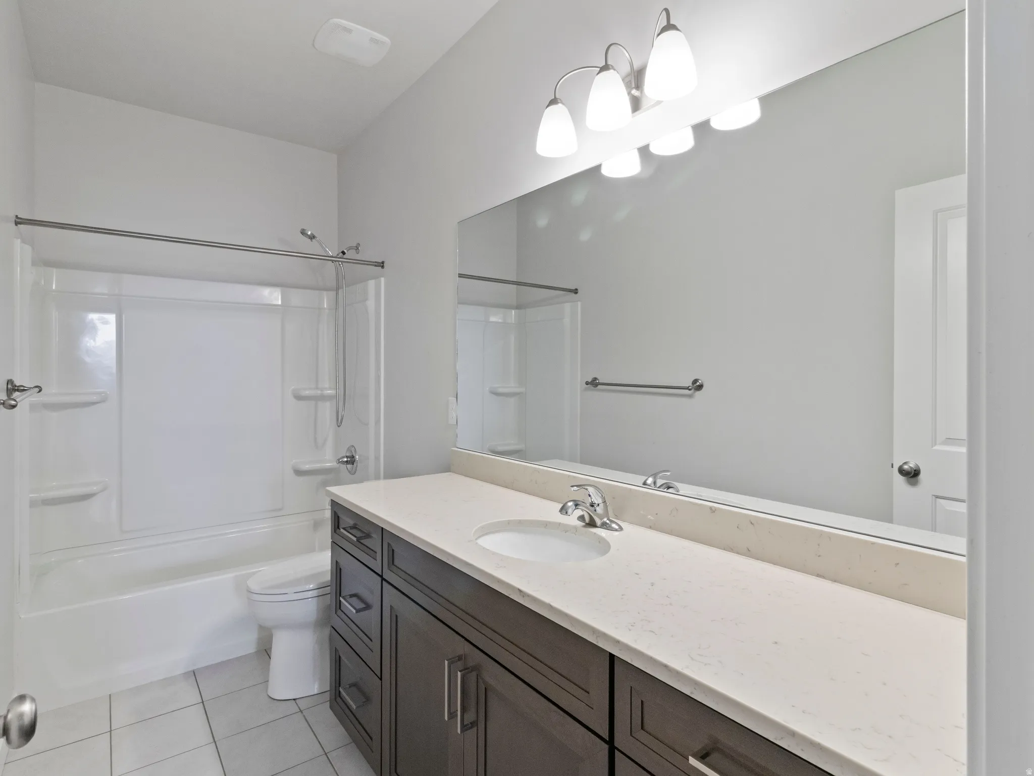 Spacious bathroom featuring a white tub and shower combination, a long vanity with dual under-mount sinks, a light-colored countertop, and a large wall-mounted mirror