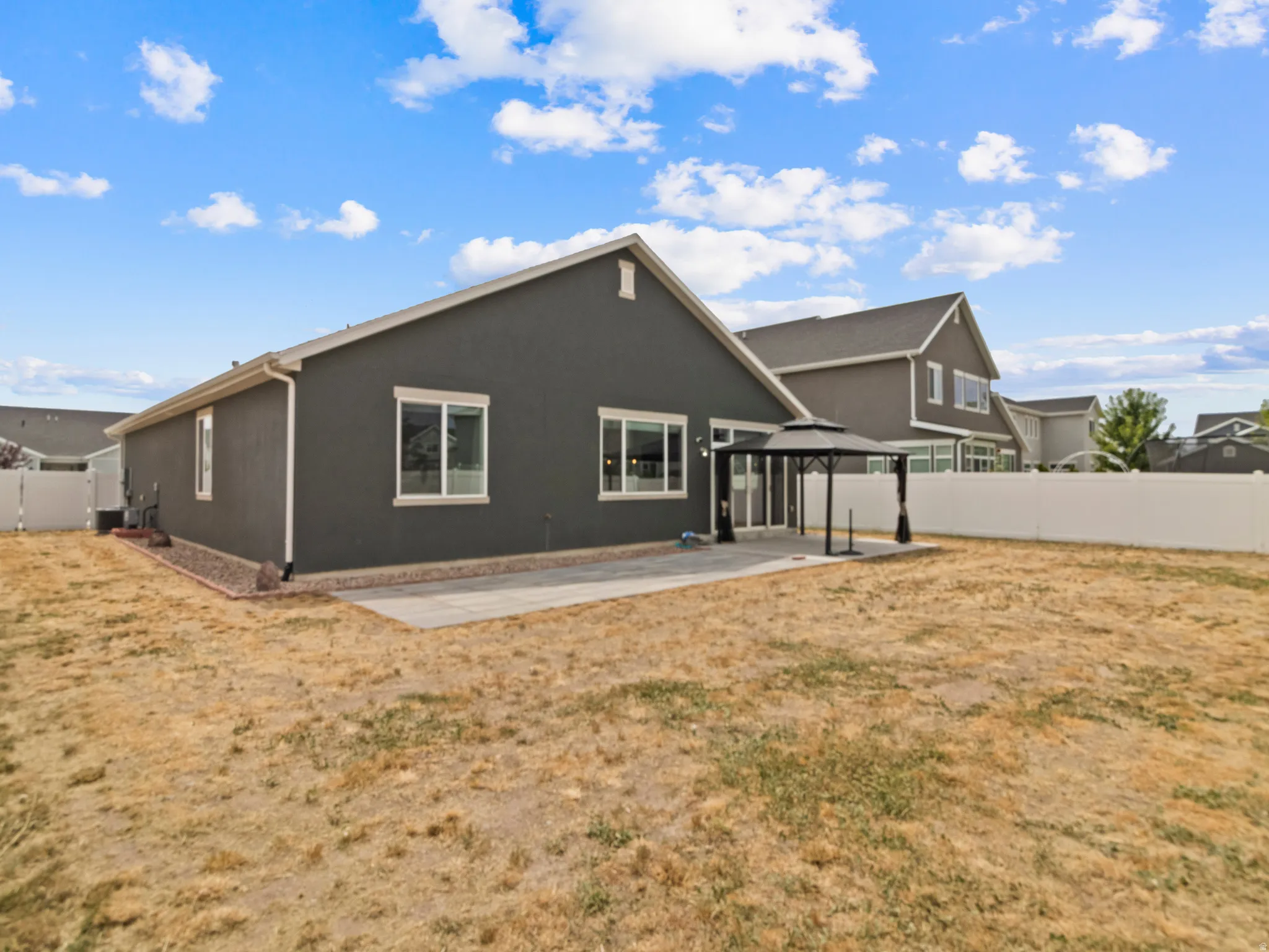 Spacious backyard featuring a concrete patio, vinyl fencing, and a dark stucco exterior
