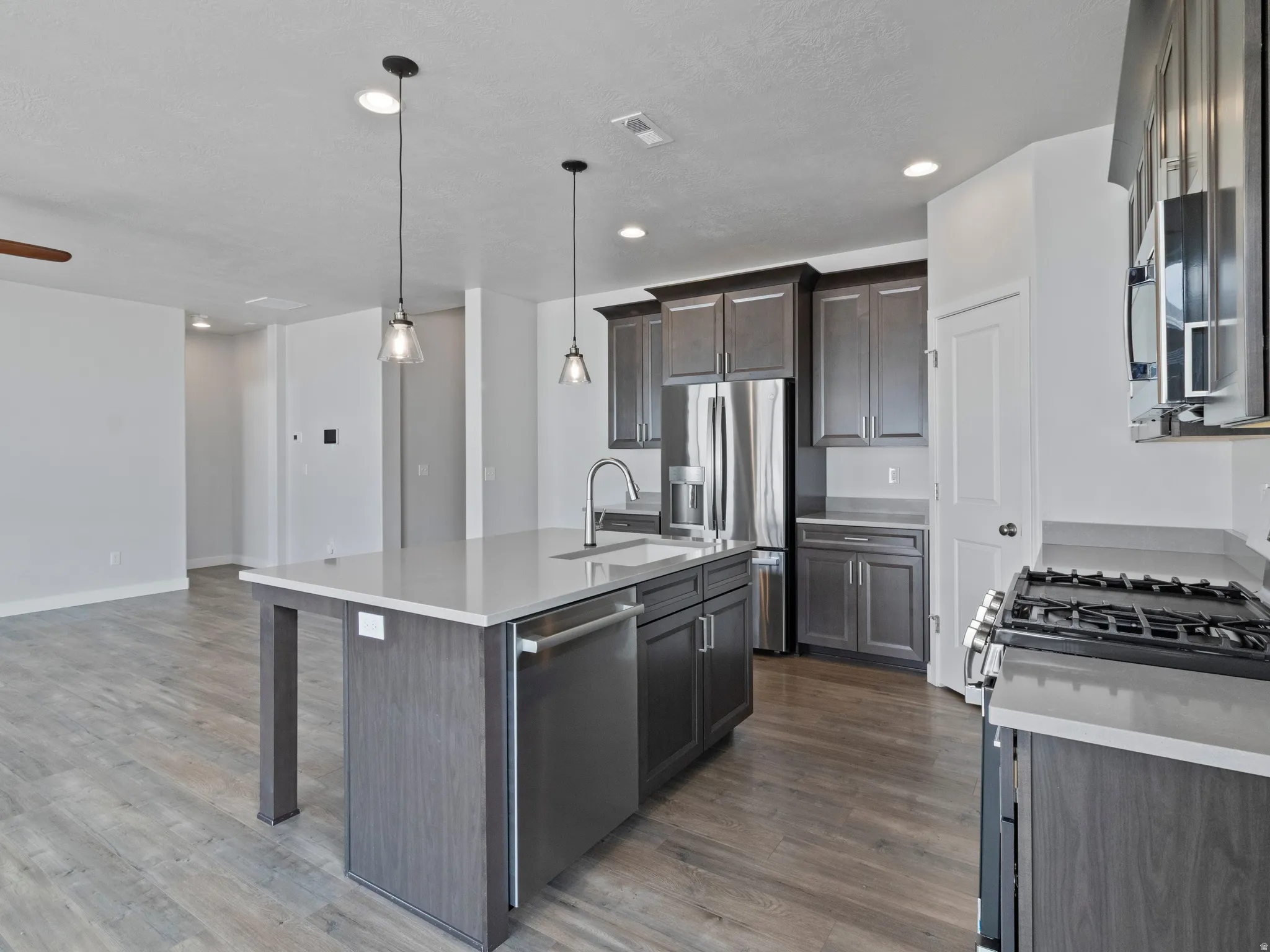 Kitchen featuring a center island, stainless steel appliances, dark wood-finish cabinetry, light-toned countertops, and wood-finish flooring