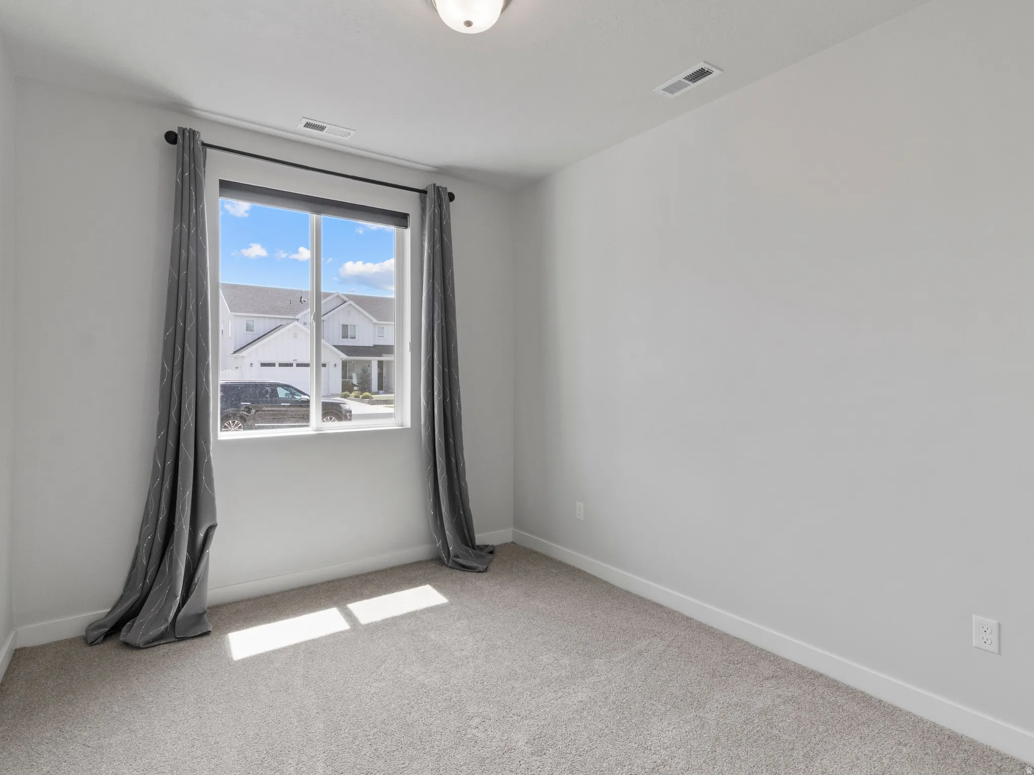 Carpeted flooring, neutral wall paint, single light fixture, window with roller shade