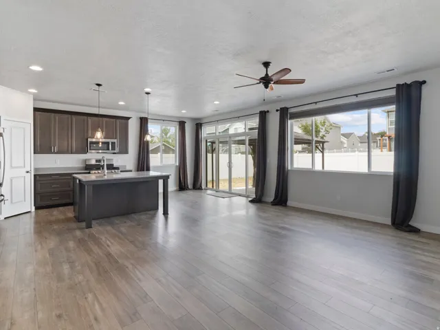 Open-concept living space featuring wood-finish flooring, a kitchen island with pendant lighting, stainless steel appliances, and large windows with sliding glass door access to the exterior