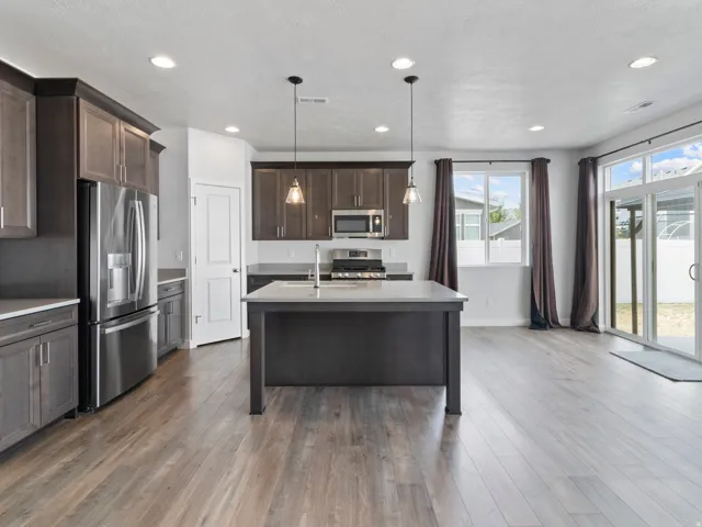 Kitchen featuring dark wood-finish cabinetry, stainless steel appliances, a center island with pendant lighting, recessed ceiling lights, and wood-finish flooring