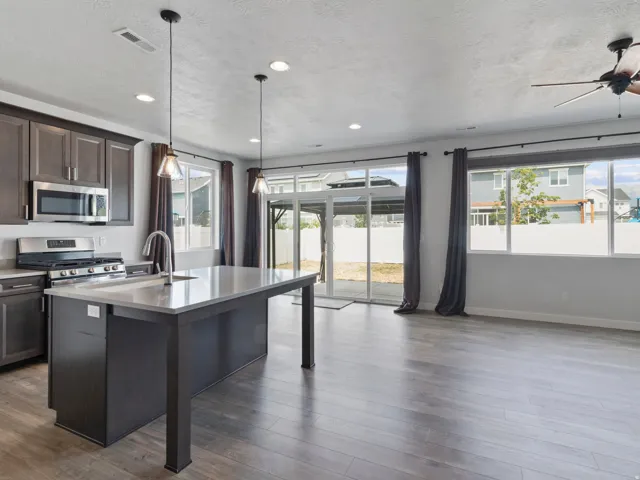 Kitchen island with integrated sink, stainless steel appliances, wood-finish flooring, recessed lighting, and large sliding glass doors