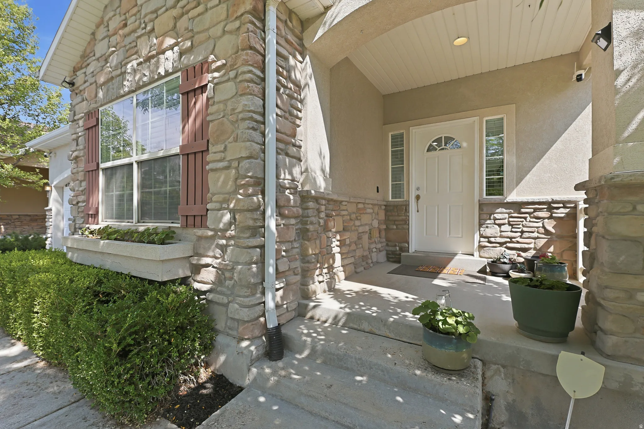 Welcoming covered entry portico with stone veneer exterior, featuring mature shrubs and seasonal plantings