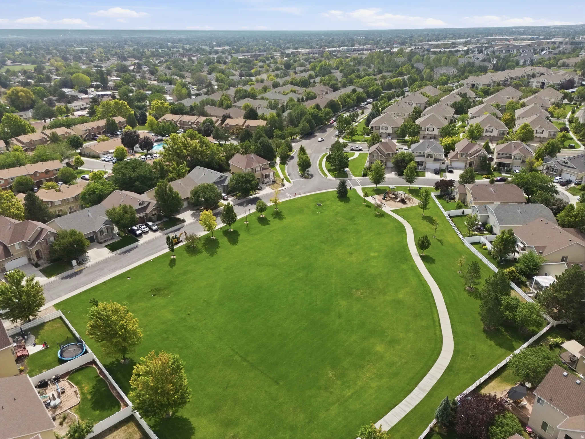 Residential community setting, featuring mature landscaping, curved hardscape pathways, and tree-lined perimeter