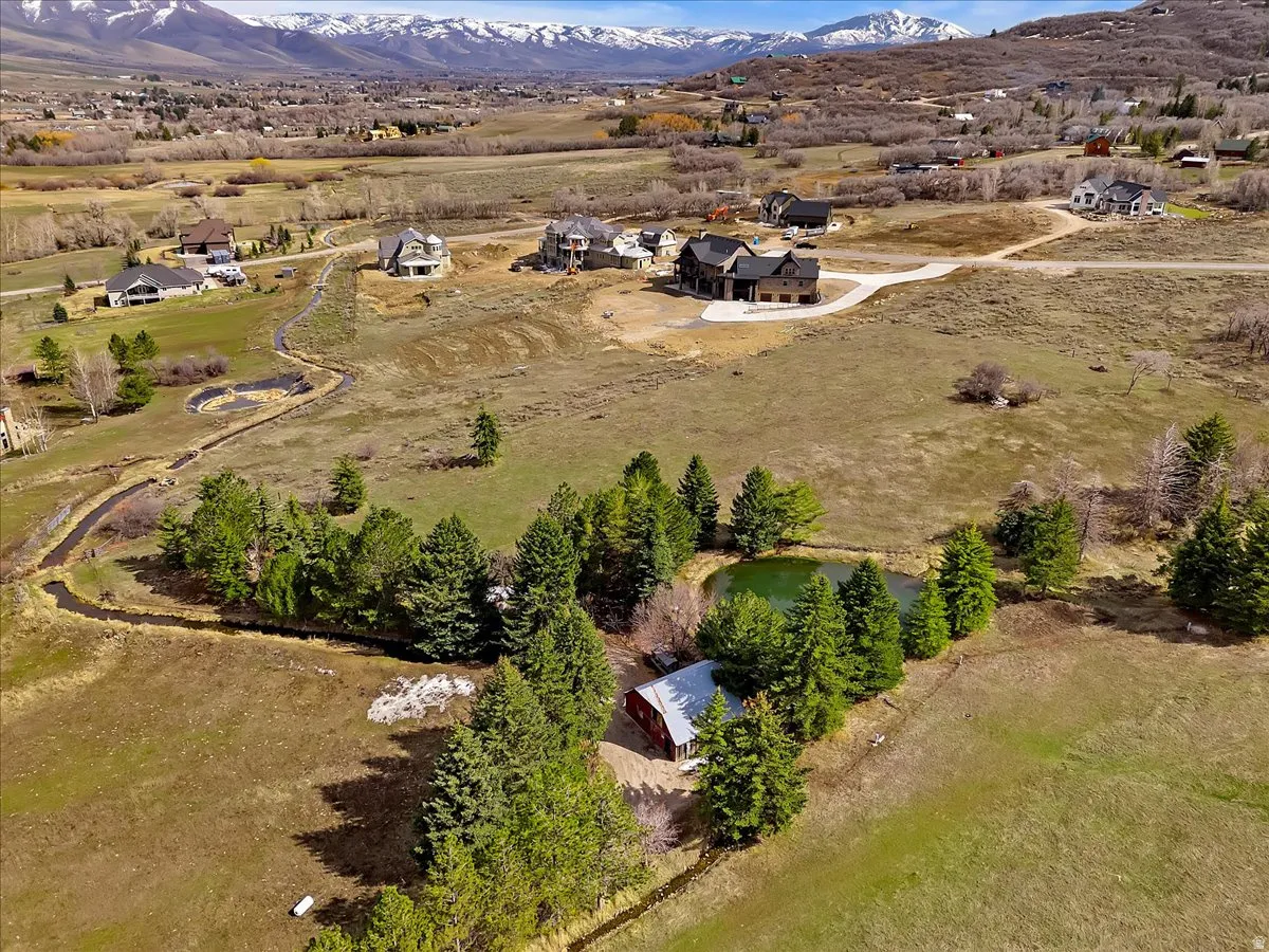 Expansive property featuring a tranquil pond, mature evergreen trees, a meandering stream, a red barn structure, and mountain scenery