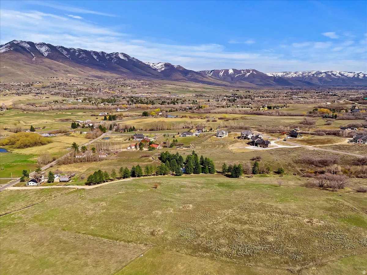 Expansive landscape with a mountainous backdrop, featuring scattered residential properties, natural terrain, and distant water features under a clear sky