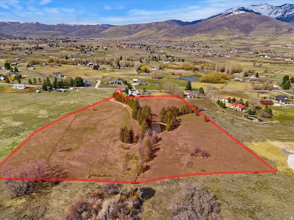 Expansive parcel featuring a defined boundary, natural pond, mature trees, and mountainous scenery