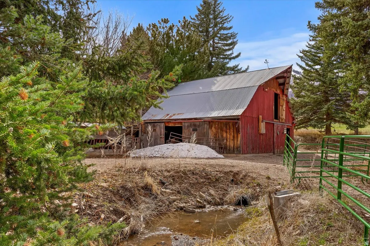 Red barn with a corrugated metal roof and a weather vane, surrounded by mature evergreen trees