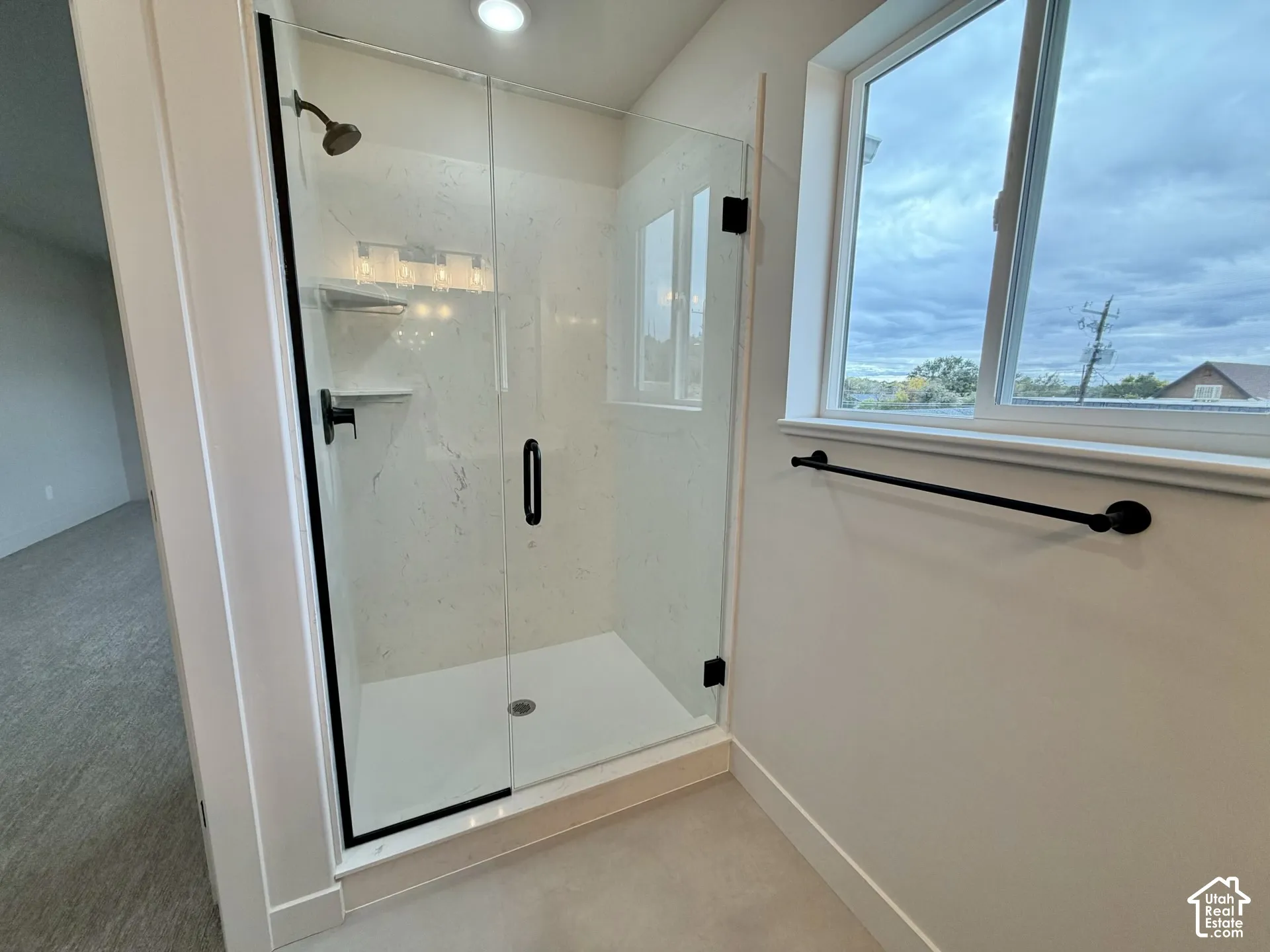 Walk-in shower featuring a frameless glass door, matte black fixtures, built-in shelving, and large-format panel surround