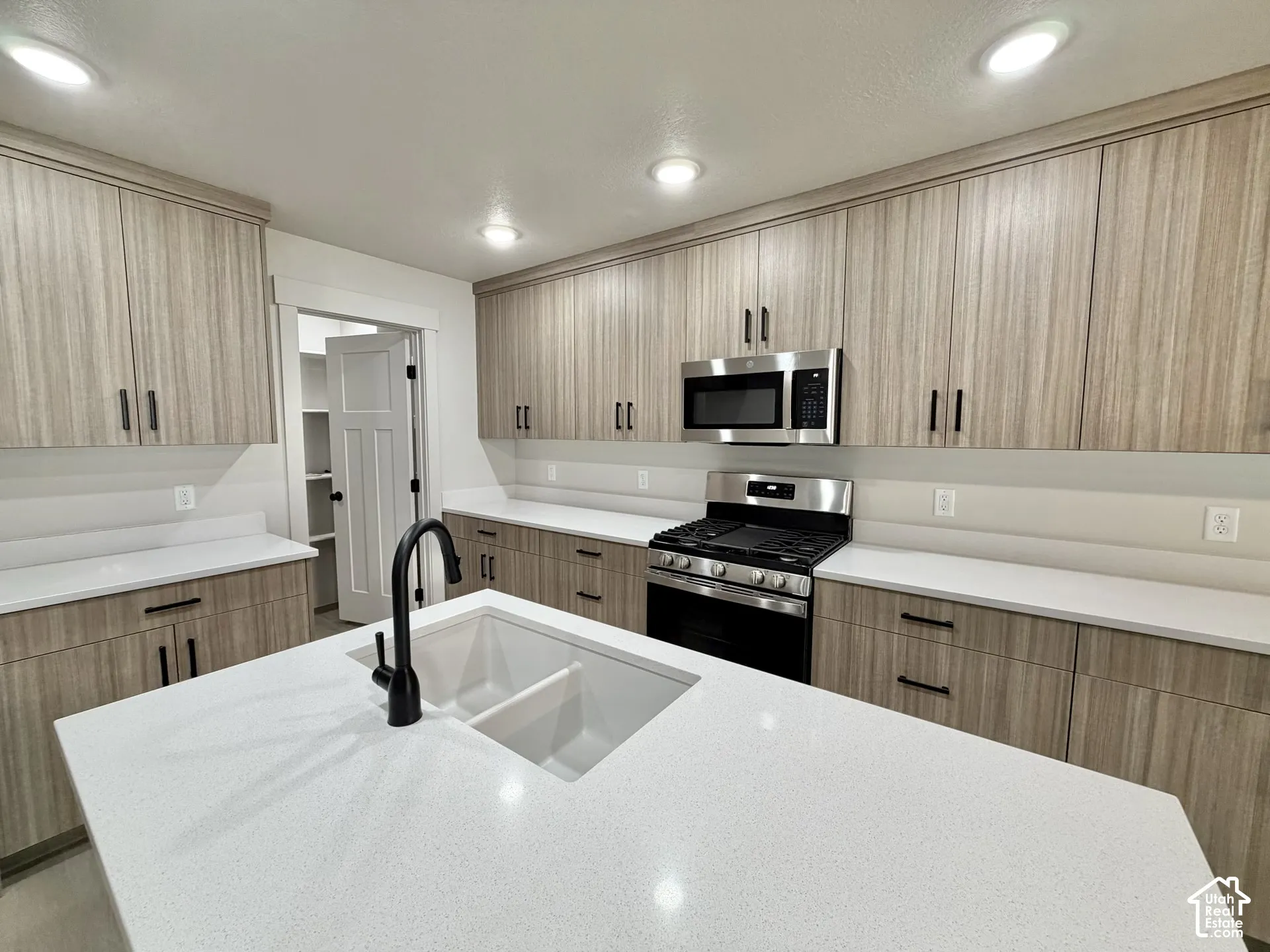 Kitchen featuring flat-panel wood-grain cabinetry, quartz countertops, a central island with an undermount dual-basin sink, matte black hardware, and stainless steel appliances