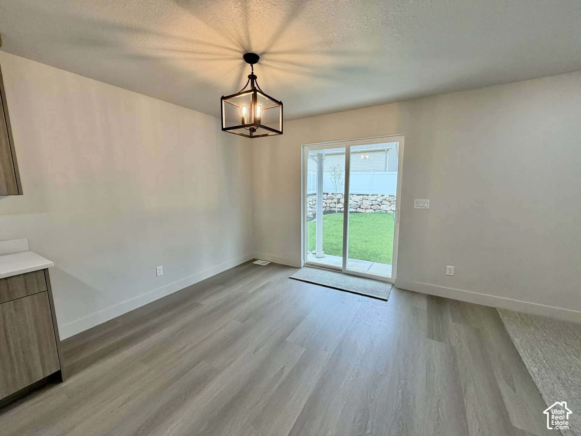 Wood-finish flooring, geometric-frame pendant lighting, glass sliding door, and kitchen cabinetry with solid-surface countertops
