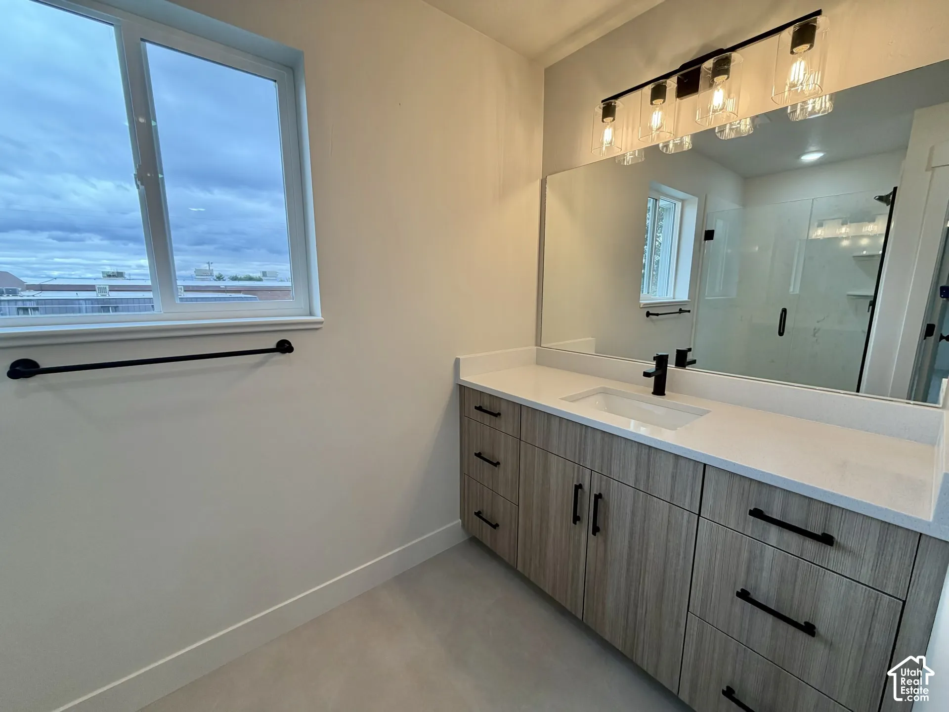 Bathroom vanity featuring wood-finish cabinetry, quartz countertop, rectangular undermount sink, matte black hardware, and an industrial-style multi-light fixture