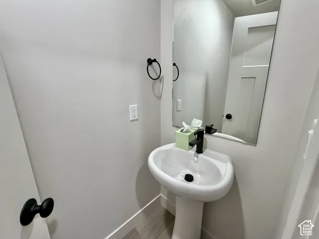 Pedestal sink with matte black faucet, wall-mounted mirror, matte black towel ring, and wood-finish flooring
