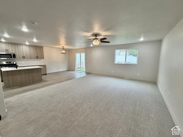 Open-concept space featuring wood-finish cabinetry, a large kitchen island with white solid-surface countertops, neutral carpeting, recessed lighting, and a sliding glass door