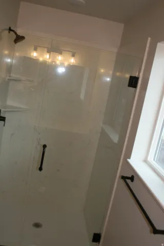 Glass-enclosed shower with a bronze-finish showerhead, integrated shelving, and a dark-finish handle