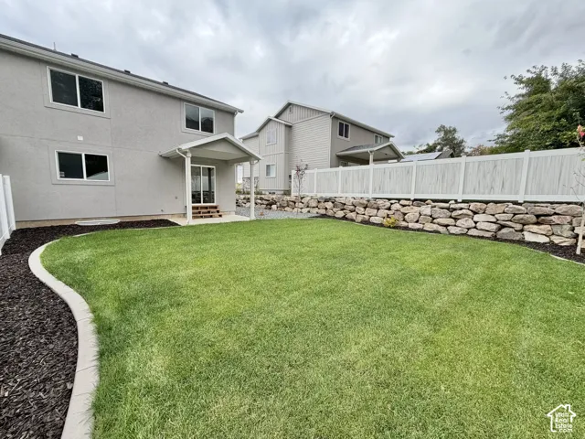 Backyard featuring a manicured lawn, stone retaining wall, concrete landscape edging, covered patio, and privacy fencing