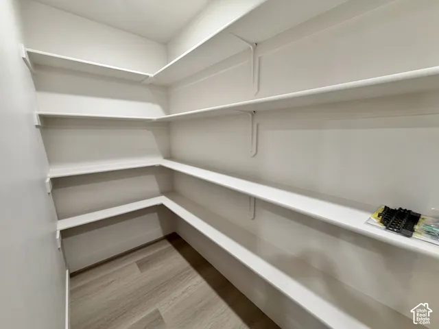 Walk-in storage space featuring wrap-around white shelving and wood-finish flooring