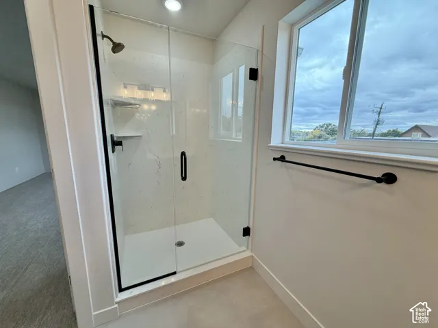 Walk-in shower featuring a frameless glass door, matte black fixtures, built-in shelving, and large-format panel surround