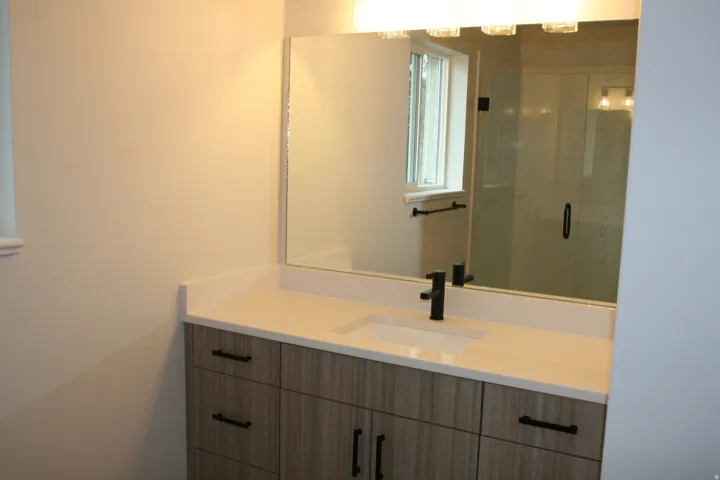 Wood-finish vanity with matte black hardware, integrated sink, and light-toned countertop