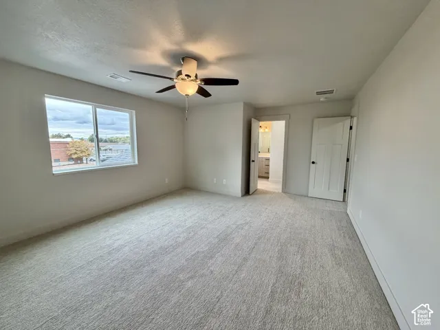 Neutral-toned interior space featuring wall-to-wall carpeting, a multi-blade ceiling fan with integrated lighting, and a multi-panel interior door
