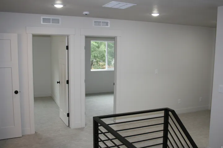 Neutral wall color, recessed lighting, white trim, light-toned carpeting, and a contemporary black metal stair railing